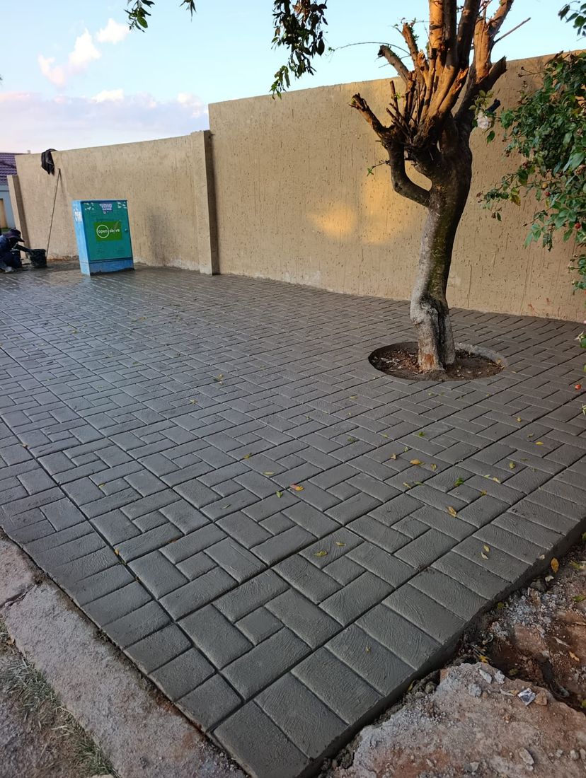 Basket-weave patterned grey concrete driveway with garden tree