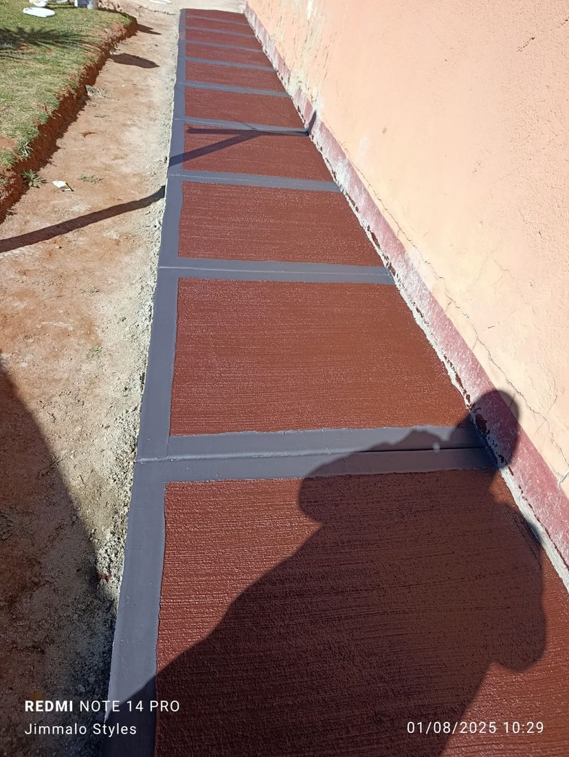 Grey-bordered terracotta scored concrete panel walkway along a boundary wall